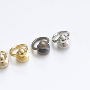 May include: Four metal rings with a ball in the center and a flat base. The rings are in different finishes: silver, brass, gold, and bronze.