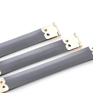 May include: Three gray straps with gold metal buckles. The buckles have a decorative design.