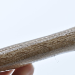 May include: Close-up of a wooden dowel rod with a smooth, light brown finish. The rod is slightly curved and has a natural wood grain pattern.