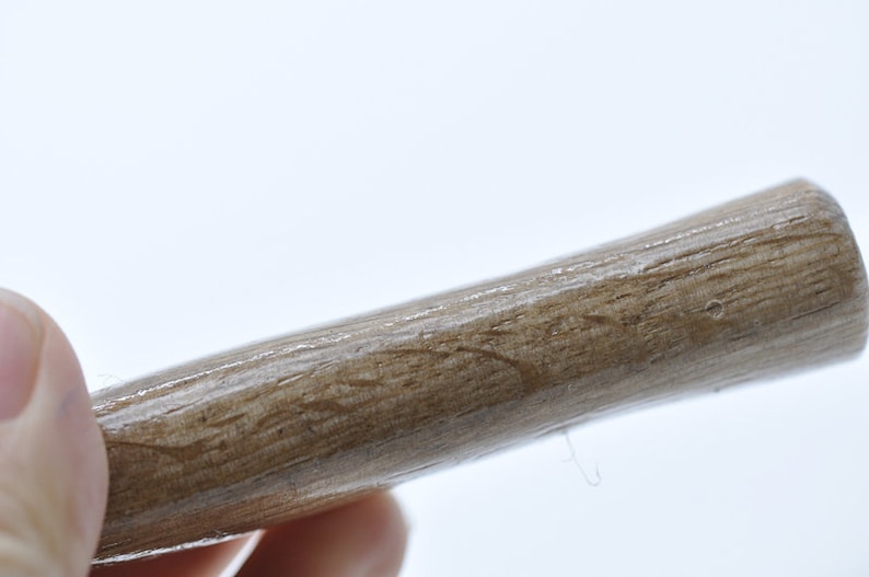 May include: Close-up of a wooden dowel rod with a smooth, light brown finish. The rod is slightly curved and has a natural wood grain pattern.
