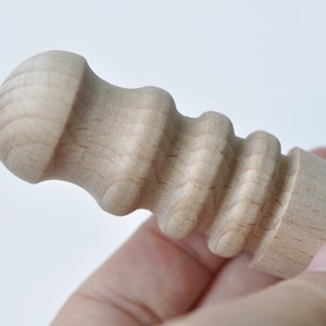 May include: Close-up of a wooden dowel with a rounded knob on one end and a textured, ridged surface on the other end.