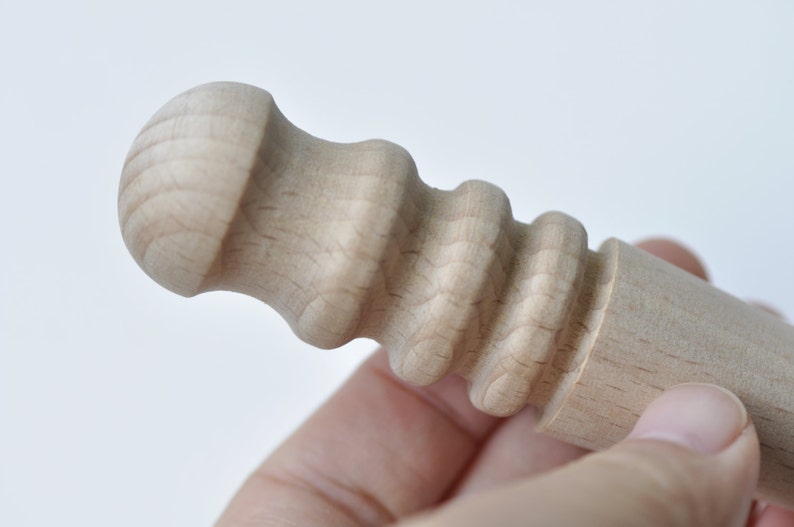 May include: Close-up of a wooden dowel with a rounded knob on one end and a textured, ridged surface on the other end.