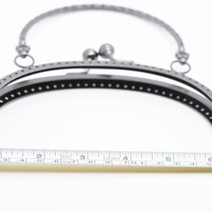 May include: A silver-toned metal purse frame with a 10-inch opening. The frame is designed to be used for crafting purses and bags.