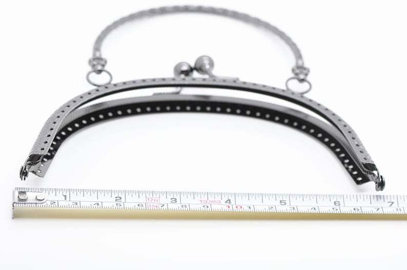 May include: A silver-toned metal purse frame with a 10-inch opening. The frame is designed to be used for crafting purses and bags.