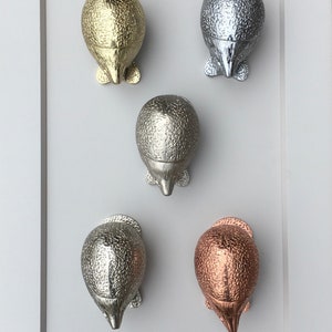 May include: Five decorative door knobs in the shape of a hedgehog. The knobs are made of metal and have a textured finish. The knobs are in different colors: gold, silver, nickel, copper, and bronze.