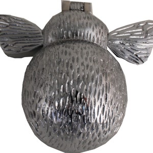 Op de afbeelding: Een zilveren deurklopper in de vorm van een bij met een textuur. De klopper heeft twee vleugels en een rond lichaam.