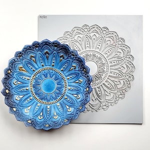 Puede incluir: Un diseño de mandala azul y dorado en un plato de cerámica. El plato es un molde para crear un diseño decorativo.
