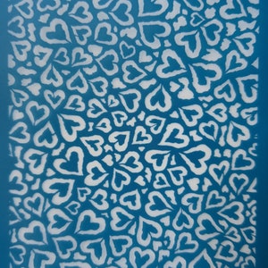 Op de afbeelding: Een blauwe stencil met een patroon van witte harten. De stencil heeft de tekst "T's 21" en "moiko" erop.