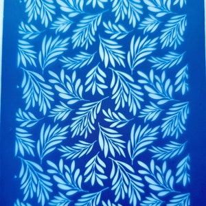 Op de afbeelding: Blauwe plastic sjabloon met een wit bladmotief. De sjabloon heeft de tekst "moiko 19.22" in de linkerbovenhoek en "moiko" in de rechterbenedenhoek.