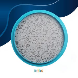 Puede incluir: Un cortador de galletas redondo gris con un diseño floral y de gallos detallado, enmarcado en un marco azul claro. El cortador presenta intrincados patrones recortados y el nombre de la marca "moiko" en la parte inferior.