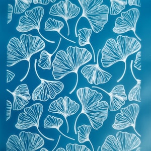 Puede incluir: Una estera de horneado de silicona azul con un patrón de hojas de ginkgo blanco. La estera tiene el texto "eo.er oxiom" impreso en la esquina superior derecha y "oxiom" impreso en la esquina inferior izquierda.