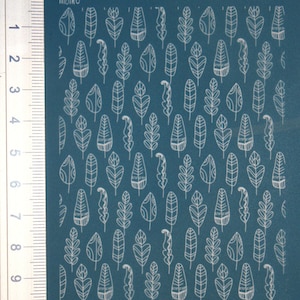 Op de afbeelding: Een vel wit zelfklevend papier met een teal achtergrond en een herhalend patroon van witte omlijnde bladeren. Het vel is gemarkeerd met een liniaal aan de linkerkant.