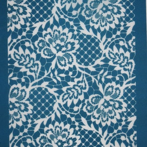 Könnte beinhalten: Eine weiße Spitzen-Schablone auf einem blaugrünen Hintergrund. Die Schablone zeigt ein sich wiederholendes Muster aus floralen Designs.