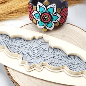 May include: A white silicone mould with a detailed design of a floral pattern. The mould is used for creating decorative elements for crafts and baking.