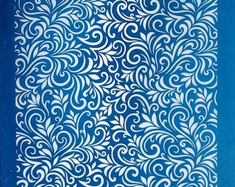 May include: A blue stencil with a white intricate floral pattern. The stencil has the text "moiko 19.35" in the top left corner and "moiko" in the bottom right corner.