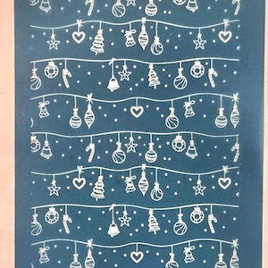 Op de afbeelding: Een vel met witte kerst-nagel stickers op een blauwe achtergrond. De stickers hebben een herhalend patroon van kerstballen, snoepstokken, sterren, bellen en kerstboom.