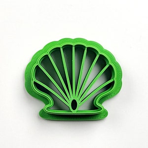 Può includere: Un tagliapasta di plastica verde a forma di conchiglia. Il tagliapasta è dettagliato e rappresenta una conchiglia.