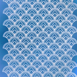 Puede incluir: Un fondo azul con un patrón blanco de formas superpuestas en forma de concha. Cada forma tiene un diseño floral delicado y una fila de pequeños círculos a lo largo del borde.