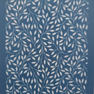 May include: A blue stencil featuring a repeating design of white leaves and branches. The stencil has the text "moiko 19.42" in the top left and "moiko" in the bottom right. Ideal for crafts and home decoration projects.