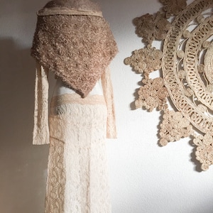 Puede incluir: Una falda larga de encaje blanco con una chal de ganchillo marrón drapeado sobre un maniquí.