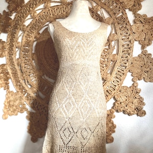 May include: A beige crochet dress with a diamond pattern. The dress is sleeveless and has a fitted bodice and a flowing skirt.