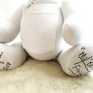 May include: A white fabric teddy bear with a rounded torso and limbs. The left foot features black handwritten text that reads "Papa" and "2018". The right foot features black handwritten text that reads "My Best Friend" with a line underneath.