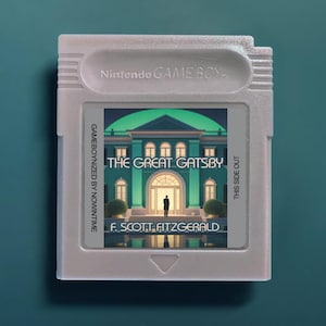 以下が含まれることがあります： 任天堂ゲームボーイのビデオゲームカートリッジ。ライトグレーの本体に、邸宅のイラストと「The Great Gatsby by F. Scott Fitzgerald」、「Gameboynized by Nowintime」、「This Side Out」という文字が印刷されたカスタムラベルが貼られています。