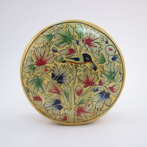 Pode incluir: Um prato redondo de cerâmica amarelo com um desenho pintado à mão de um pássaro empoleirado em um galho com flores verdes, vermelhas e azuis.