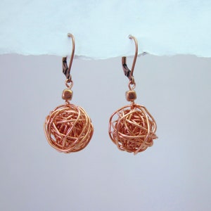 May include: A pair of copper wire earrings with a spherical shape. The earrings are made of a single piece of wire that is twisted and woven together to create a ball shape.