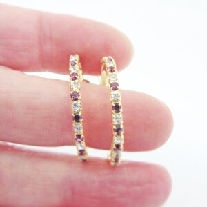 May include: A pair of gold hoop earrings with a row of clear and purple rhinestones.