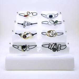 May include: Eight bracelets with different designs and colored stones. Each bracelet is made of metal and has a black elastic band.