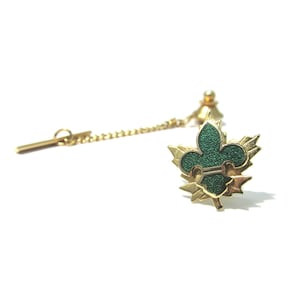 May include: Gold tie tack with a green enamel fleur-de-lis surrounded by gold leaves.