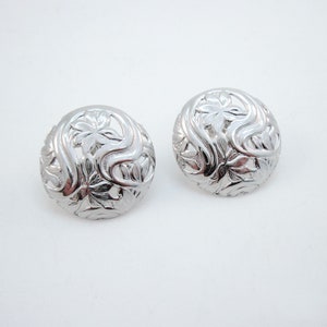 May include: A pair of silver earrings with a floral design. The earrings are round and have a delicate, intricate pattern.