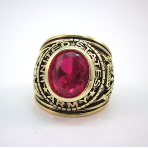 May include: A gold ring with a red gemstone and the inscription "UNITED STATES ARMY" around the band.