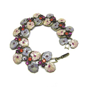 May include: A delicate bracelet featuring a floral design with pastel pink, purple, and white enamel flowers accented with sparkling pink, red, and purple rhinestones. The bracelet is made of a gold-toned metal.