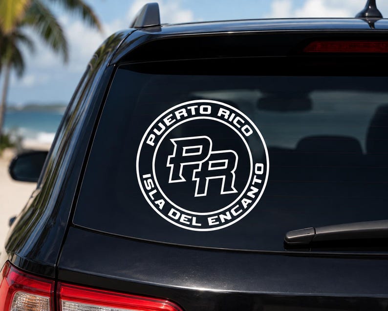May include: A circular white vinyl decal applied to a car rear window. The design features the letters PR in the center, surrounded by a circular border containing the text PUERTO RICO and ISLA DEL ENCANTO in a bold, sans-serif white font.