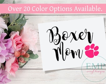 May include: A white rectangular sign featuring the black text Boxer Mom and a bright pink paw print. The text Over 20 Color Options Available appears at the top. A circular logo with the text EMP vinyl designs is in the bottom right corner.