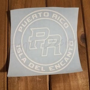 May include: A white vinyl decal featuring a circular design with the text Puerto Rico at the top and Isla Del Encanto at the bottom. In the center of the circle, the letters PR are displayed in a bold, stylized font with a white outline.