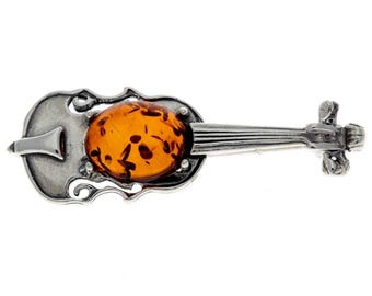 Op de afbeelding: Een zilveren viool broche met een amber steen in het midden. De viool is gedetailleerd met ingewikkelde gravures en de amber steen heeft een warme, honingachtige kleur.
