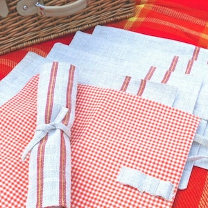 May include: A set of four placemats, two with a red and white gingham pattern and two with a solid grey colour. The grey placemats have red and yellow stripes along the edges. The placemats are rolled up and tied with a ribbon.