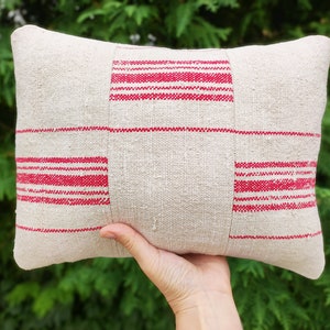 May include: A white pillow with red stripes. The pillow is made of a woven fabric and has a rectangular shape.