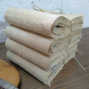 May include: A stack of four beige fabric panels, tied together with twine, on a wooden surface.