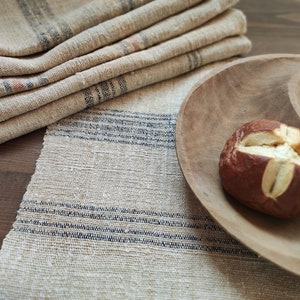 May include: A wooden serving bowl with a brown pretzel on top. The bowl is on a table with a beige and blue striped tablecloth.