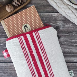 Op de afbeelding: Een witte canvas etui met rode verticale strepen en een rode rits, met daarin een vintage boek met een stippenomslag en een portretsticker. De etui heeft een klein rood-wit geruit stoffen label.