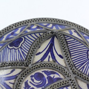 K&ouml;nnte beinhalten: Ein wei&szlig;er Keramikteller mit einem blauen und wei&szlig;en Blumenmuster. Der Teller ist mit einem silbernen Metallrand verziert.