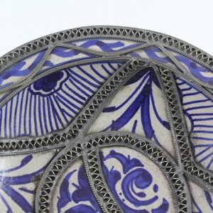 K&ouml;nnte beinhalten: Ein wei&szlig;er Keramikteller mit einem blauen und wei&szlig;en Blumenmuster. Der Teller ist mit einem silbernen Metallrand verziert.