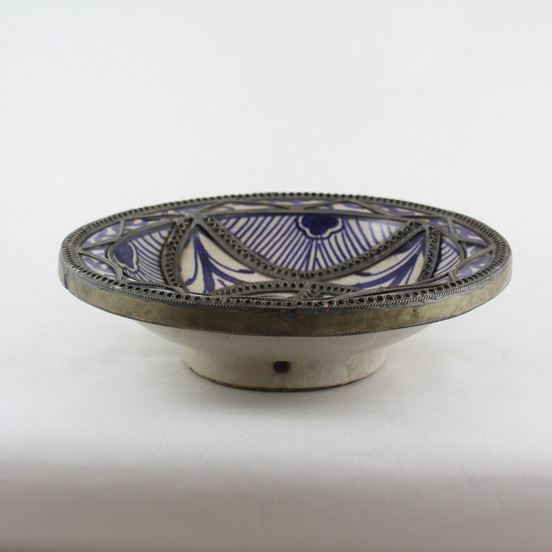 K&ouml;nnte beinhalten: Eine wei&szlig;e Keramikschale mit einem blauen und wei&szlig;en geometrischen Muster. Die Schale hat einen silbernen Metallrand und einen erh&ouml;hten Boden.