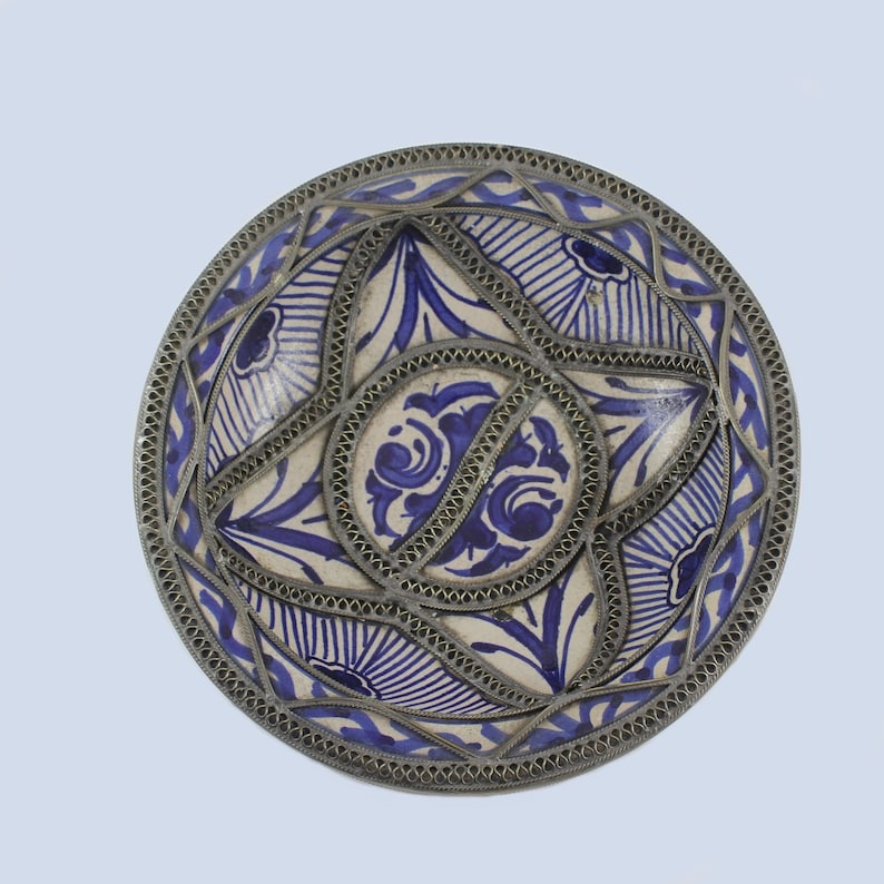 May include: A white ceramic bowl with a blue and white floral design. The bowl is decorated with a silver metal trim around the edge.