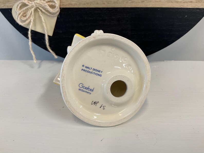 Puede incluir: Base de figura de cer&aacute;mica blanca con dise&ntilde;o circular, con el texto "WALT DISNEY PRODUCTIONS" y "Goebel W. Germany". La base tiene un agujero en el centro y el texto manuscrito "UAP 85".