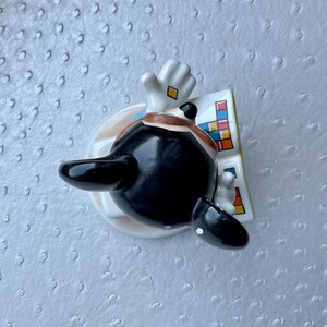 Puede incluir: Una figura de cer&aacute;mica de una figura de pelo negro con un traje, con un guante blanco y un dise&ntilde;o colorido. La figura tiene una base redonda con un dise&ntilde;o marr&oacute;n claro y azul.